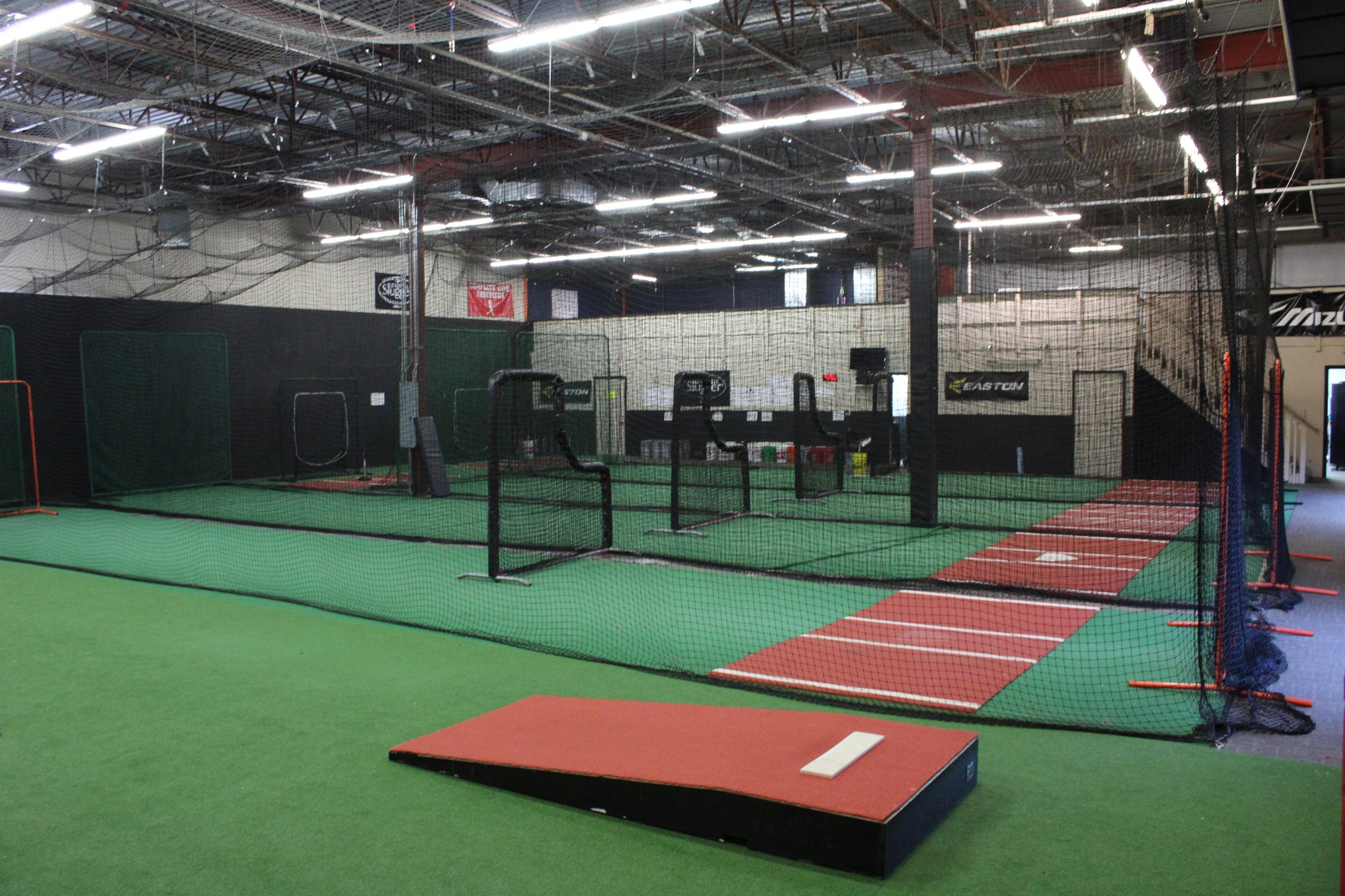 Row of netted batting cages and turf lanes inside the Complete Game training facility